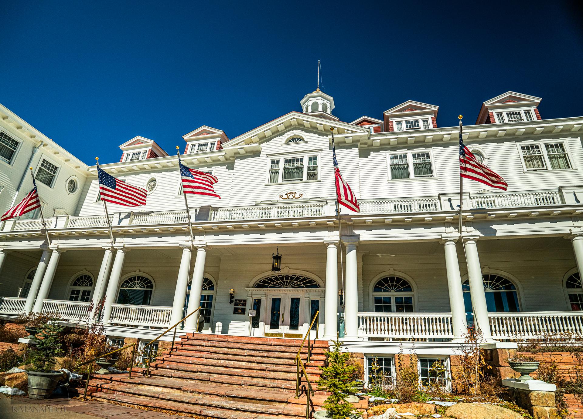 A grand white building with flags and a large porch under a blue sky.