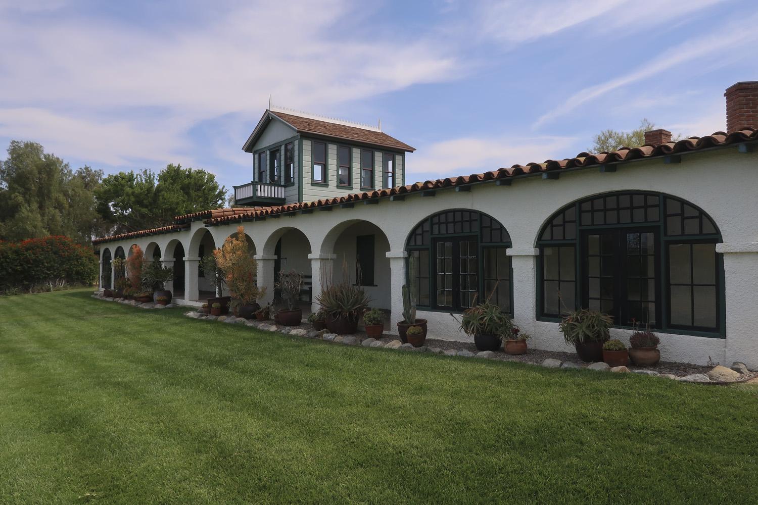 A long, white building with arched windows and a red tile roof, beside a green lawn.
