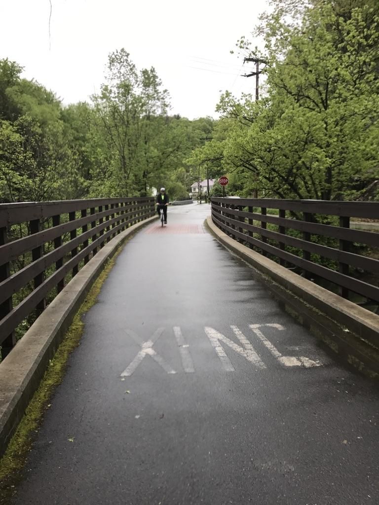 Person cycling on a paved bridge through green trees on an overcast day. - Ashuwillticook Rail Trail loop from Adams