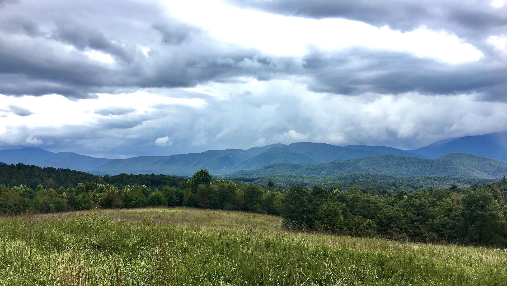 Expansive view of forested mountains under a dramatic, cloudy sky.