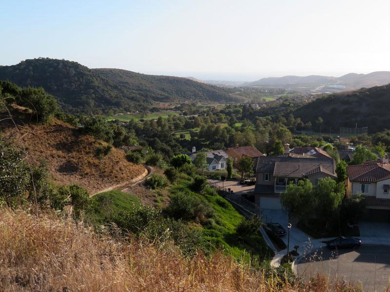 A valley landscape with houses nestled among green and dry hills under clear skies.