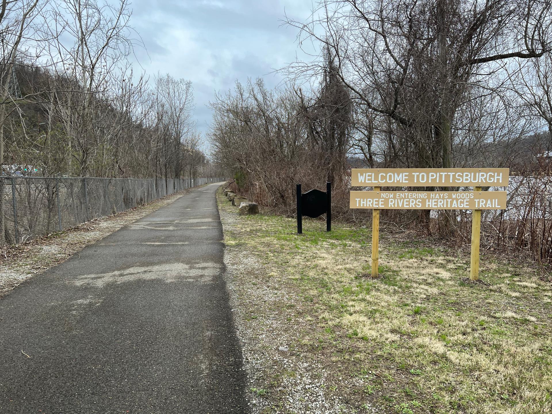 Paved trail next to a wooden sign under an overcast sky.