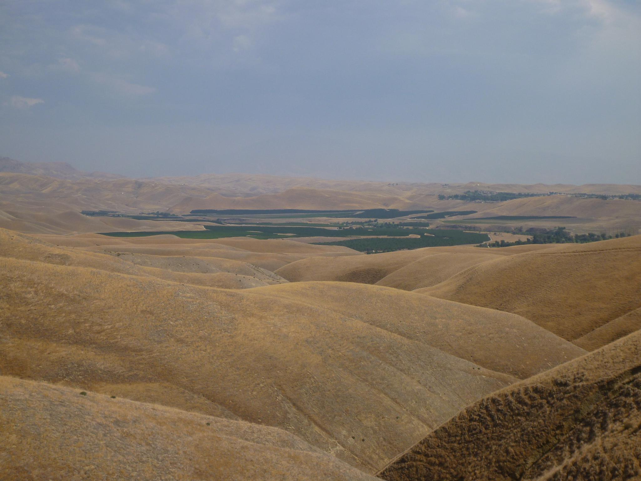 Golden rolling hills overlook a green valley under a cloudy sky.