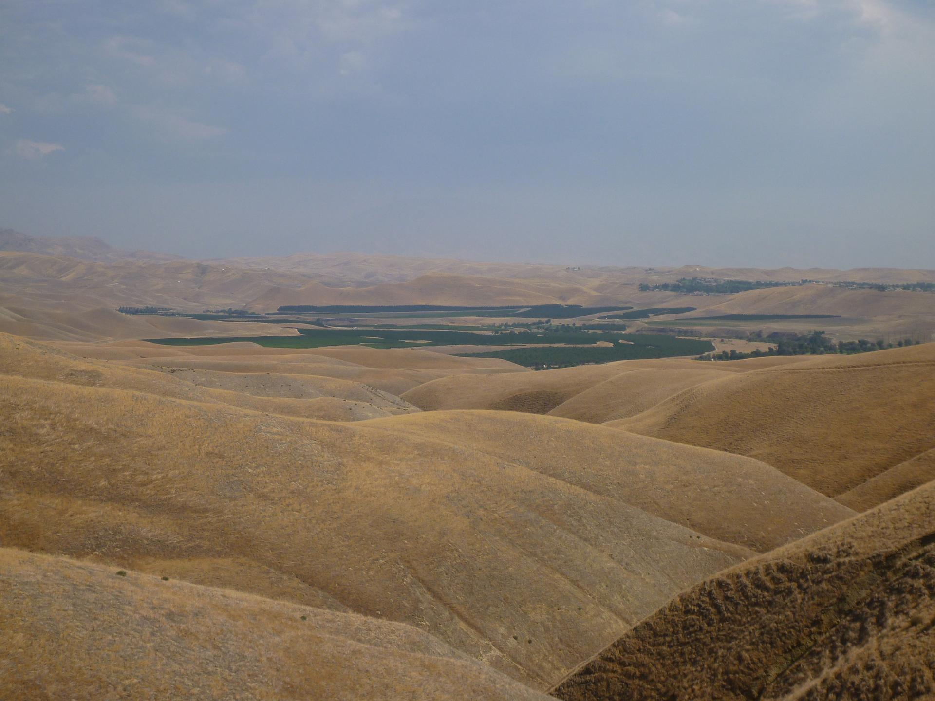 Golden rolling hills overlook a green valley under a cloudy sky.
