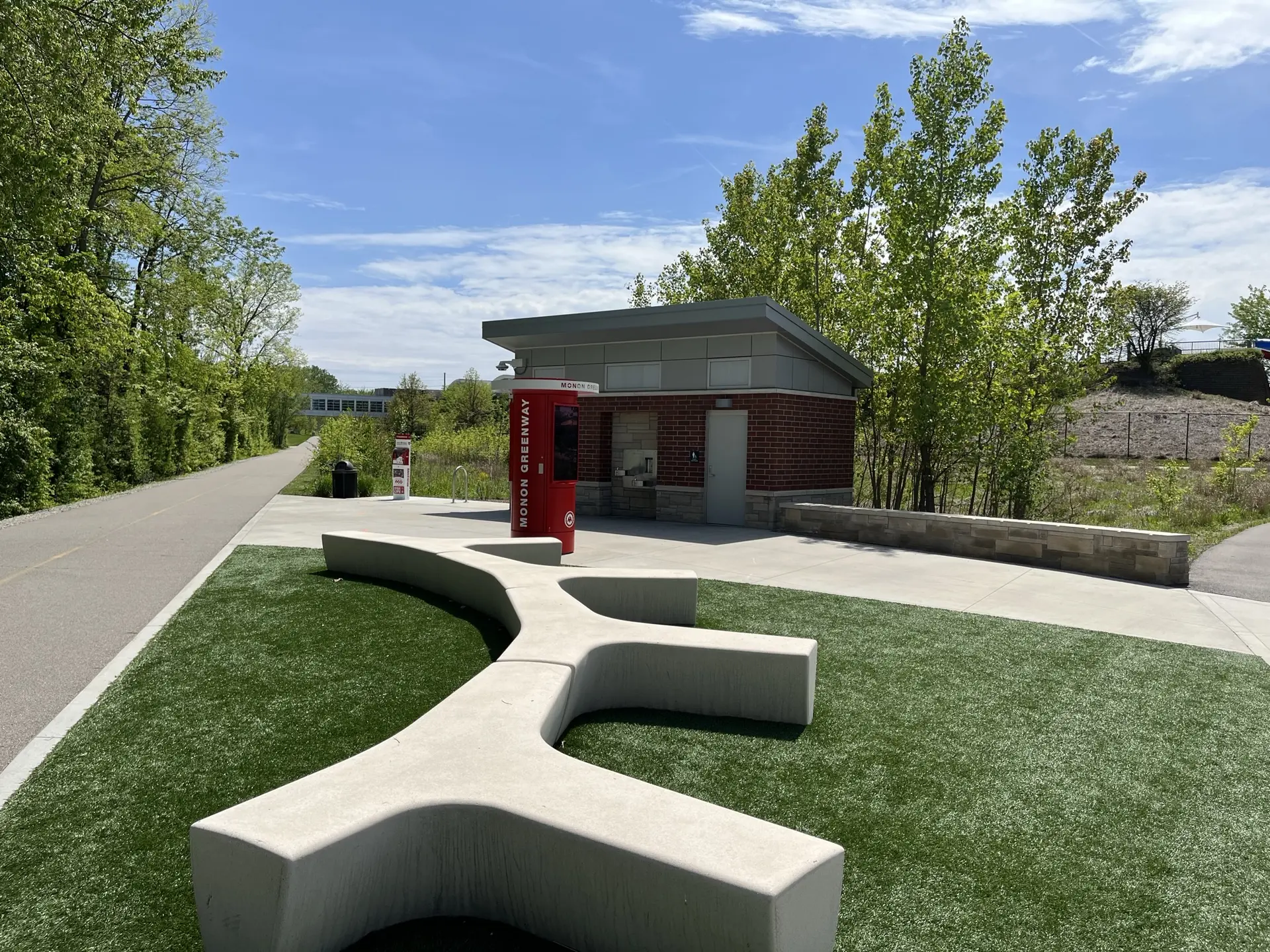 Modern concrete bench and brick building beside a paved path on a sunny day.