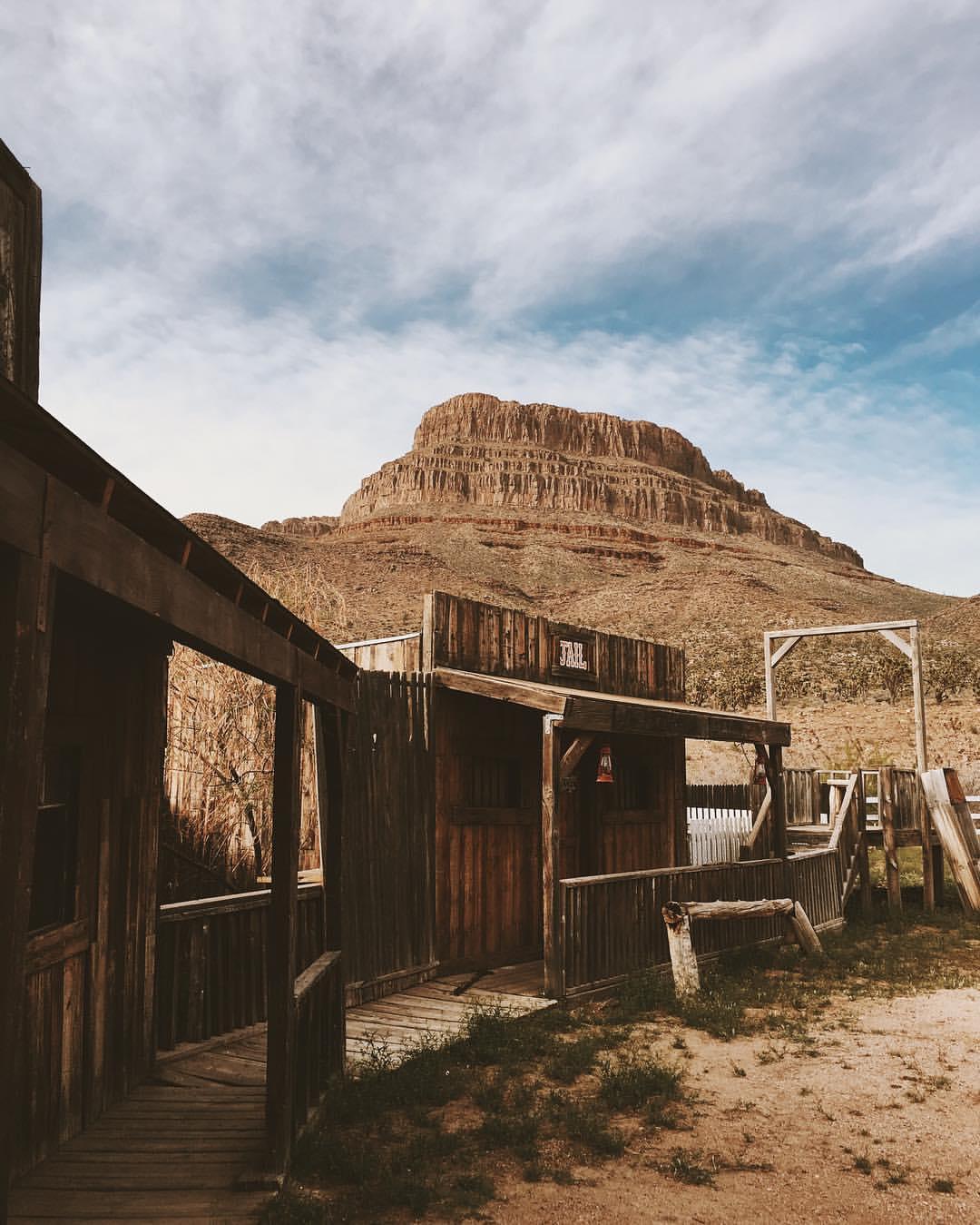 Old wooden buildings in a desert setting with a large flat-topped mountain.