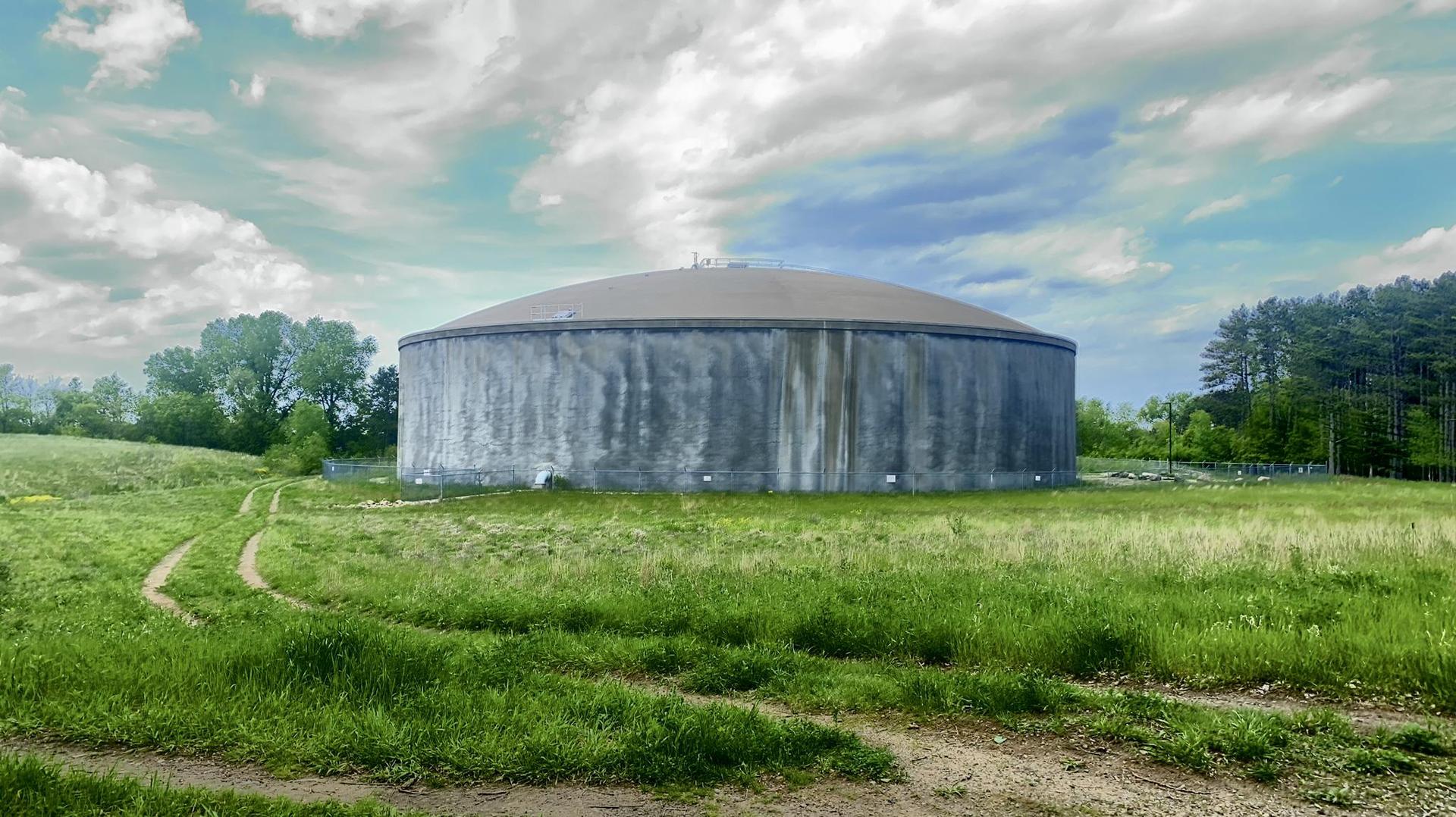 Large concrete water tank in a green field under a partly cloudy sky.