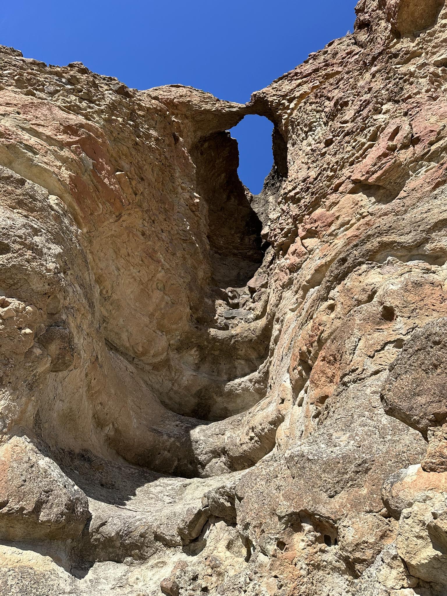 A natural rock arch in a narrow, sunlit canyon with layered walls.