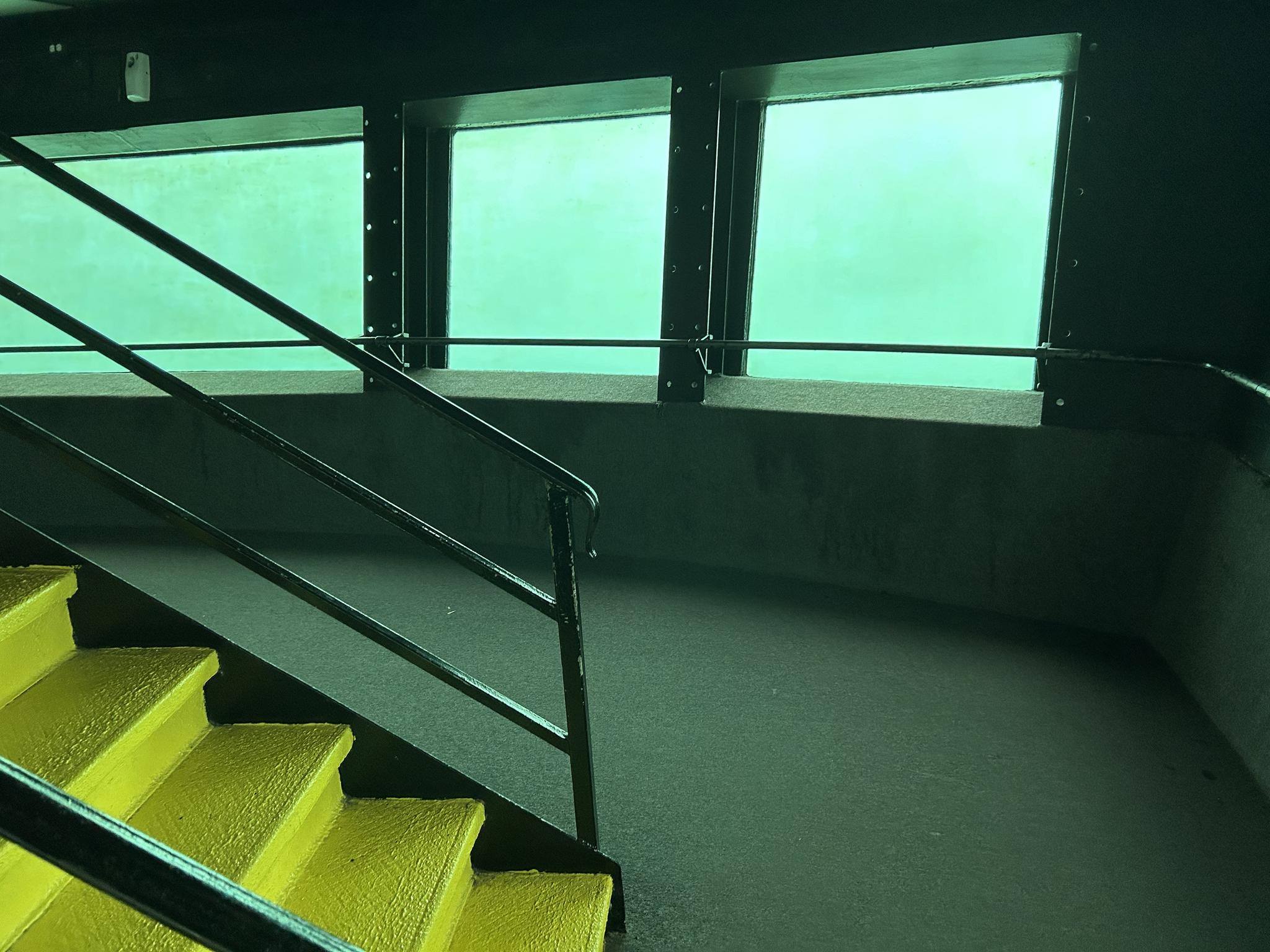 Bright yellow stairs lead to a dark room with green-tinted windows.