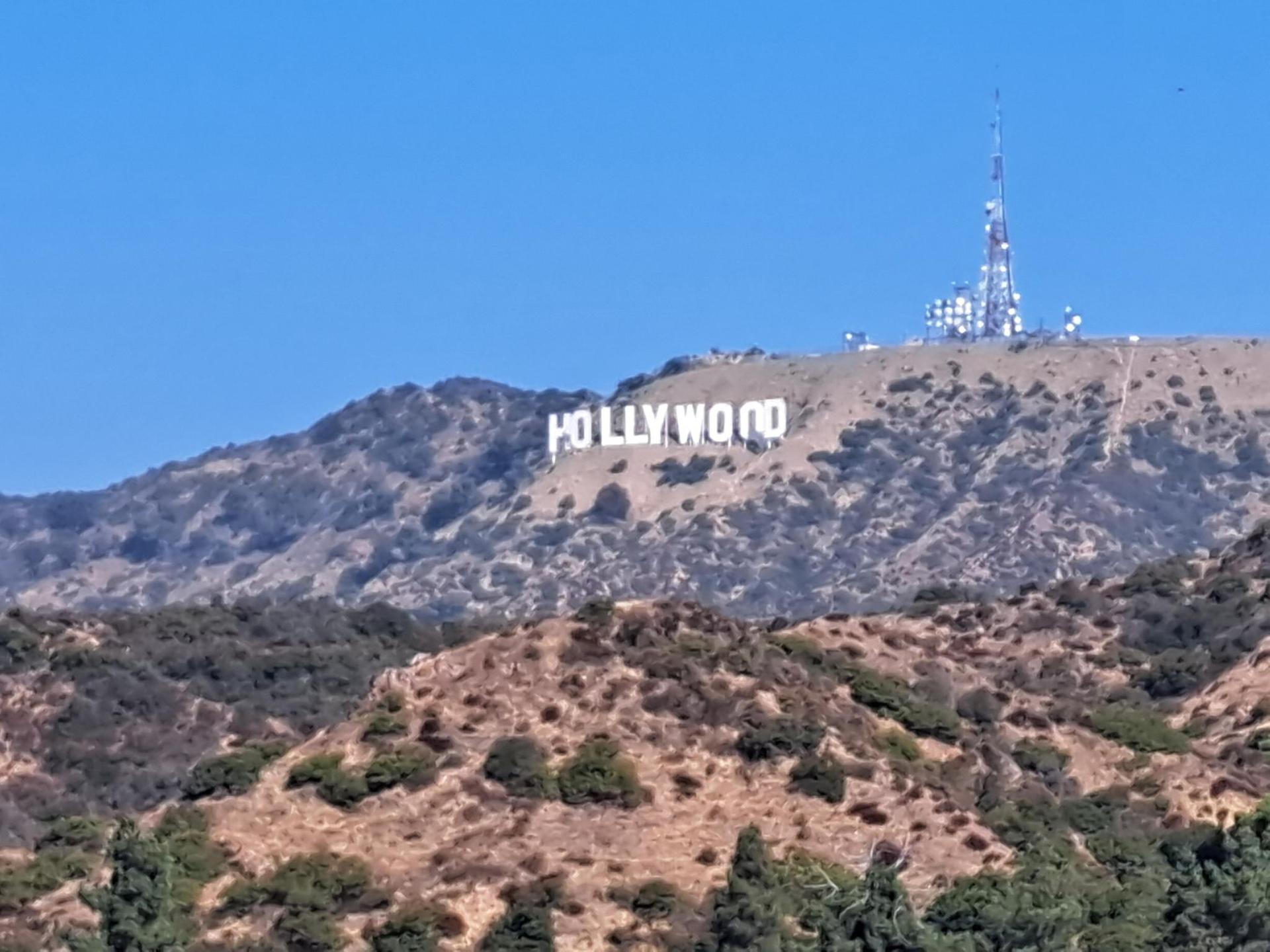 White letters on a brushy hill with a communication tower, clear sky.
