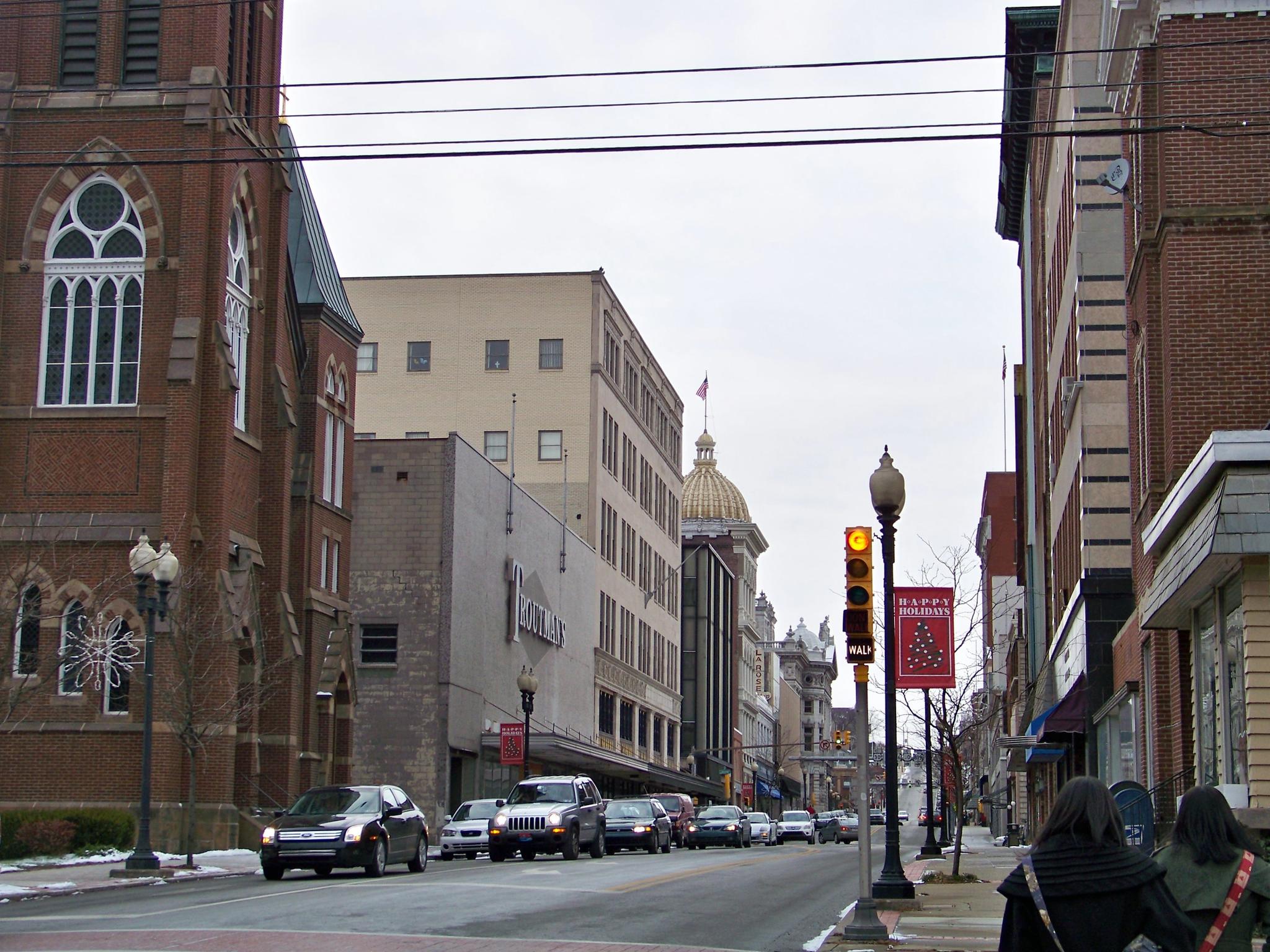 Overcast city street with historic buildings, moving cars, and pedestrians on sidewalk.