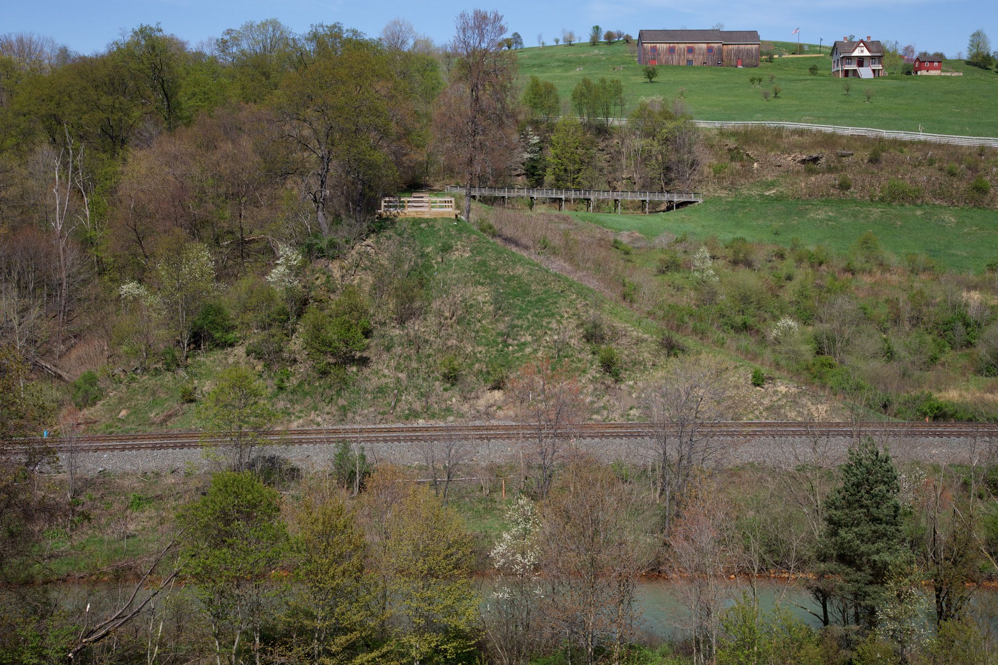 Train tracks and a river below a green hillside with distant buildings. - Path of the Flood Trail