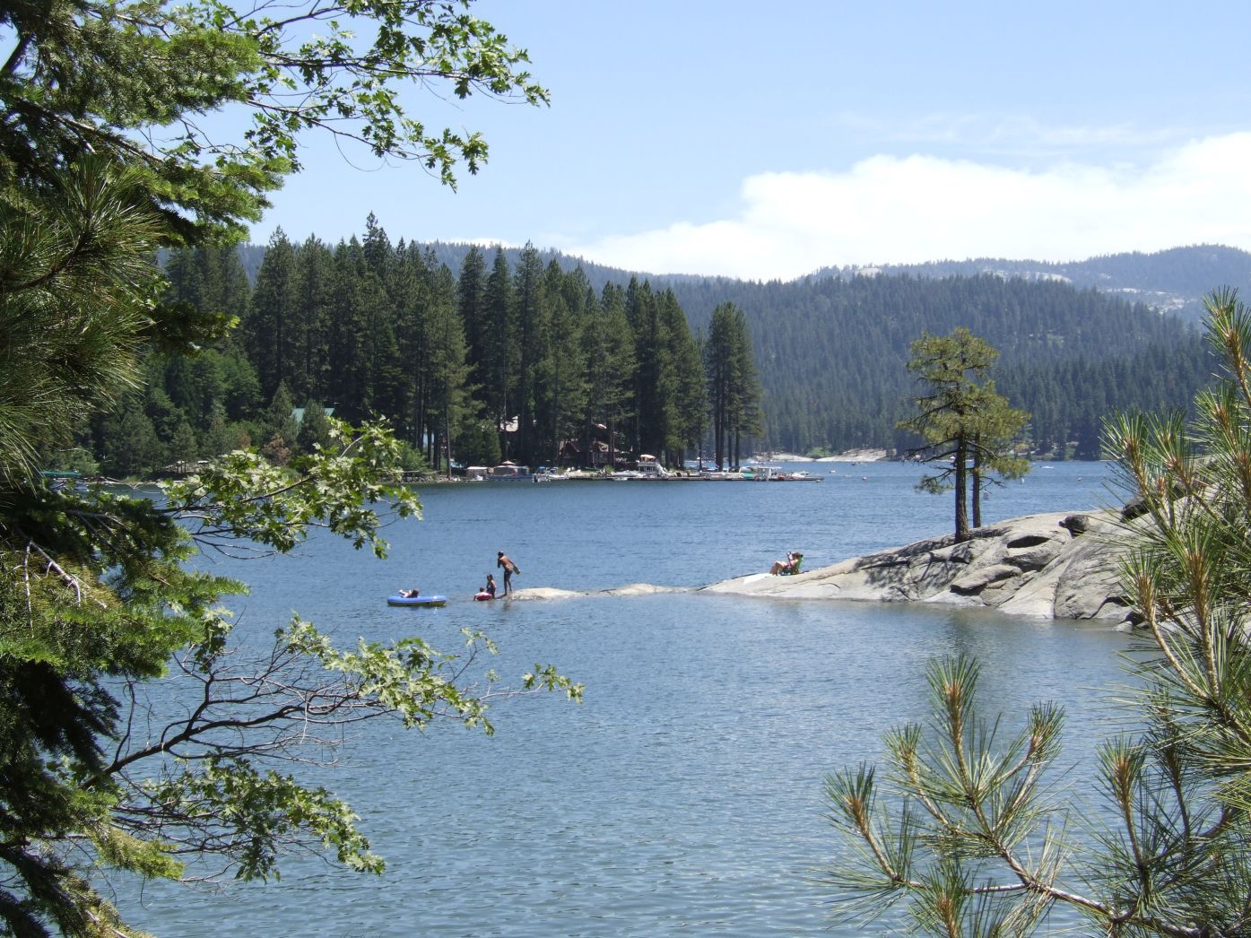 Sunny lake scene with people on paddleboards, surrounded by pine trees and hills. - Shaver Lake Perimeter Trail loop