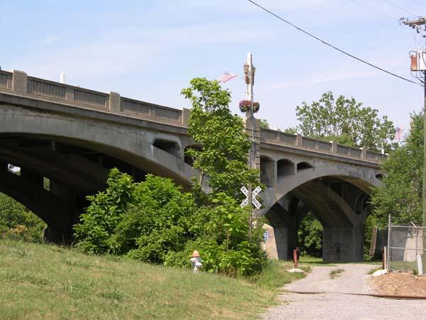 A large concrete arched bridge over a gravel path on a sunny day.