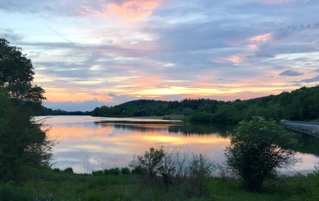 A serene lake reflects a colorful sunset sky with forested hills.