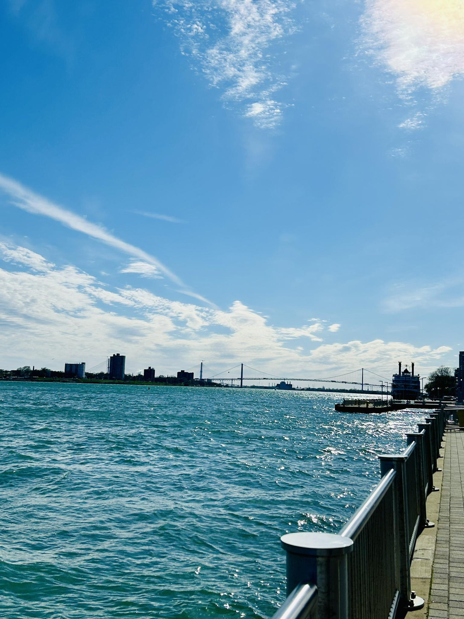 Waterfront promenade next to a wide river with a distant city skyline.