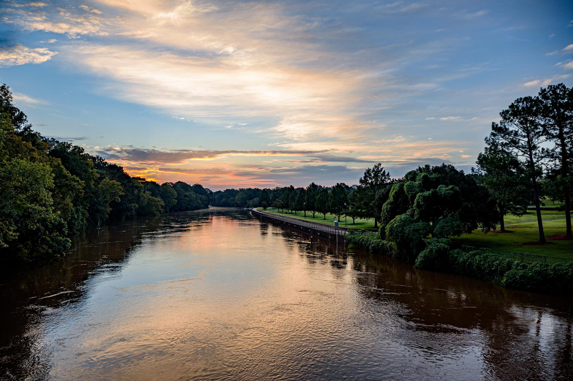 Wide river reflecting warm sunset colors, flanked by lush green trees.