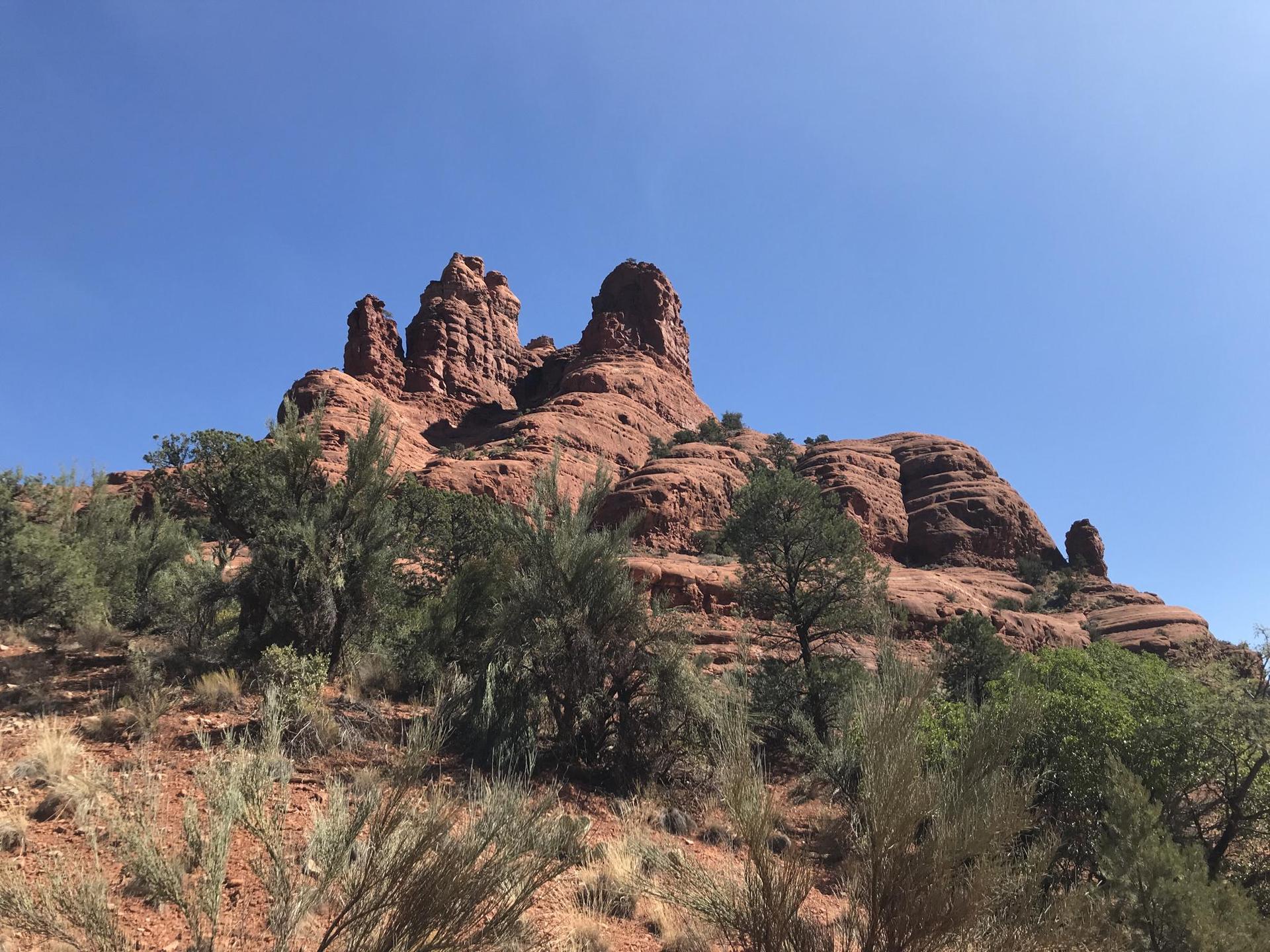 Towering red rock formations with scattered green trees under a clear sky.