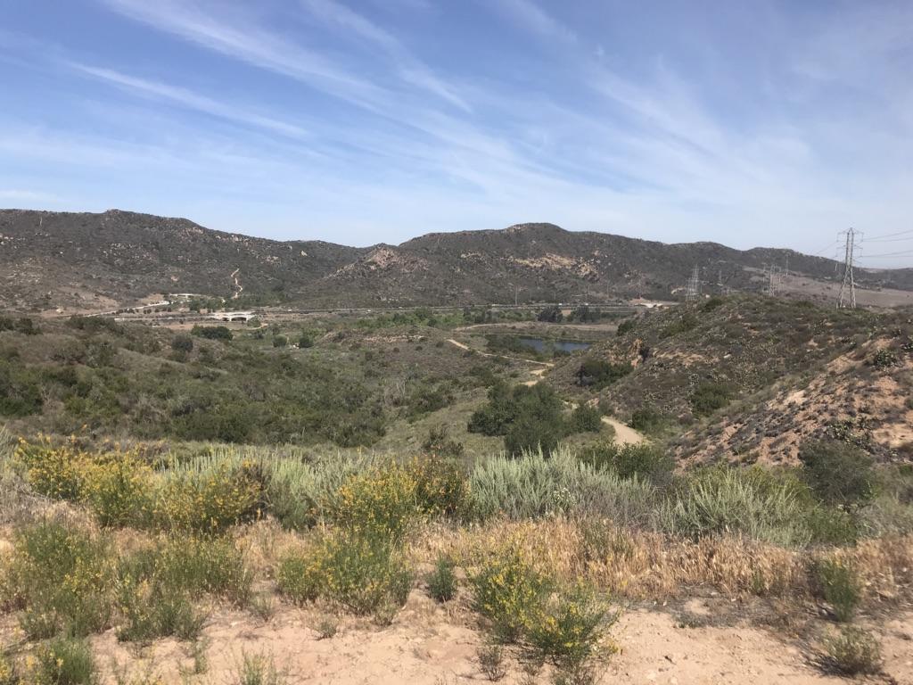 Expansive view of a valley with hills, a small lake, and power lines.