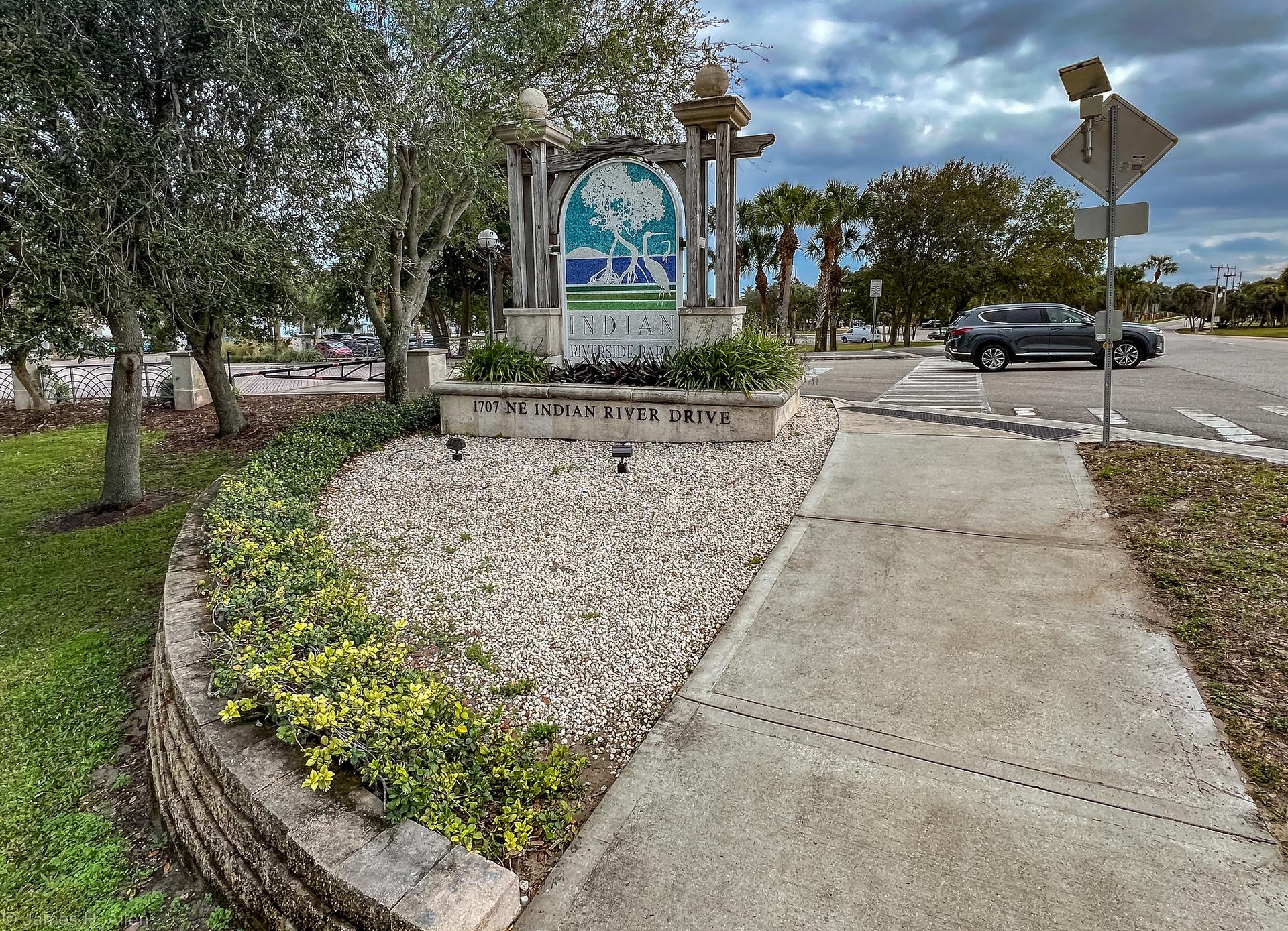A stone monument and landscaped area next to a sidewalk and road.