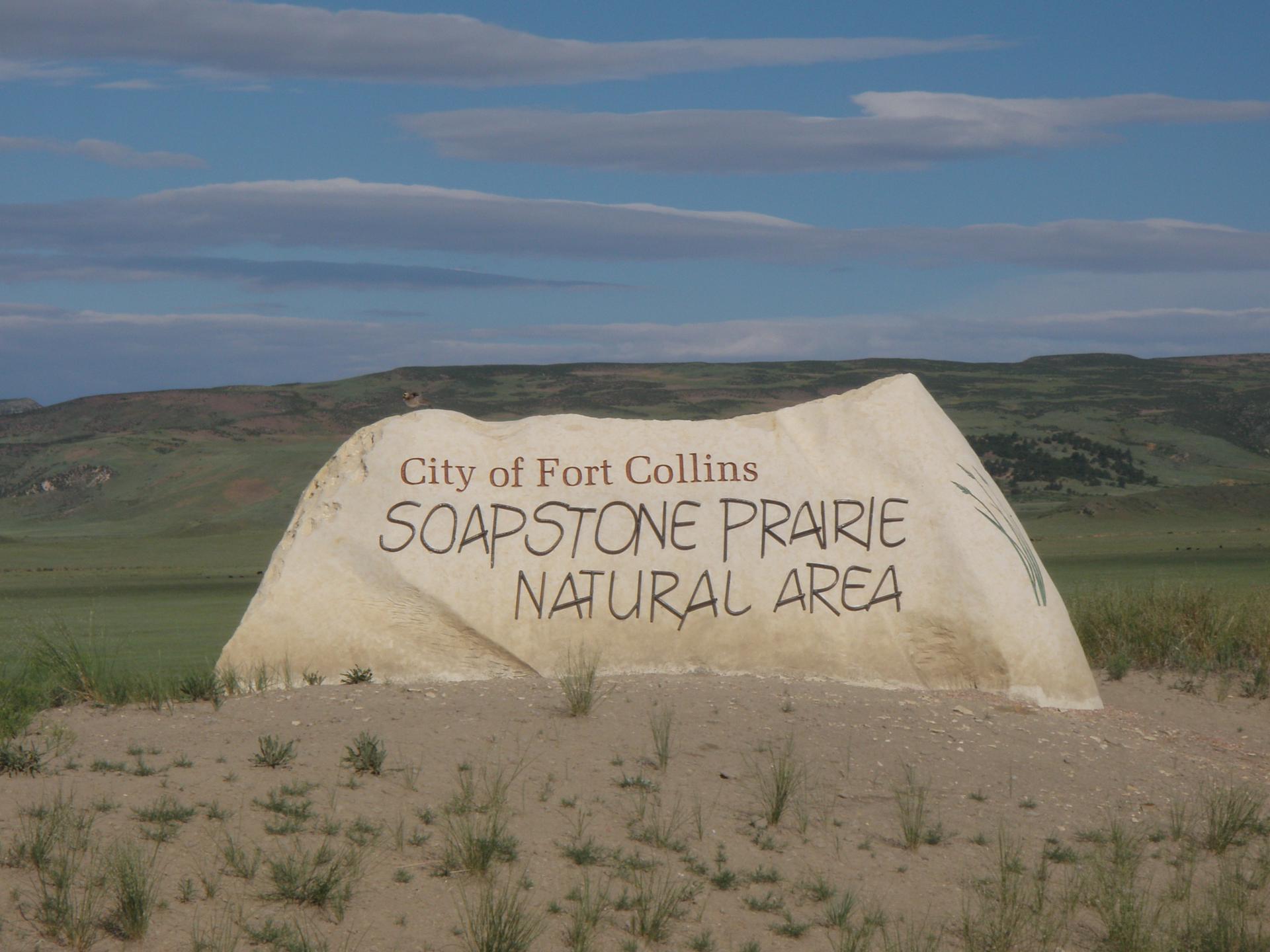 Large light-colored sign on a grassy mound under a partly cloudy sky.