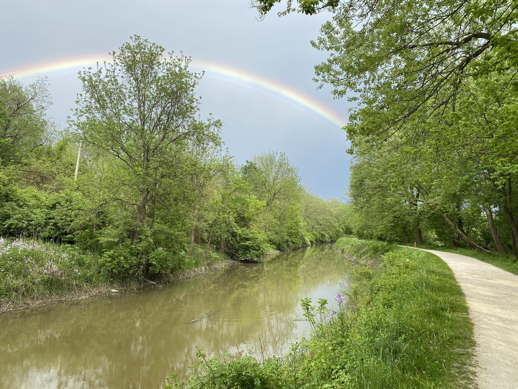 A vibrant rainbow arches over a calm river lined with lush green trees. - Ohio & Erie Canal Towpath Trail