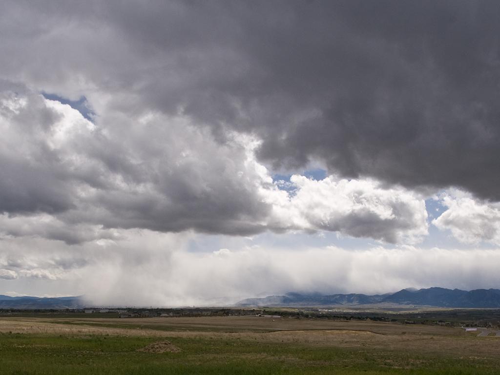 Vast plains under dark, stormy clouds with distant rain.