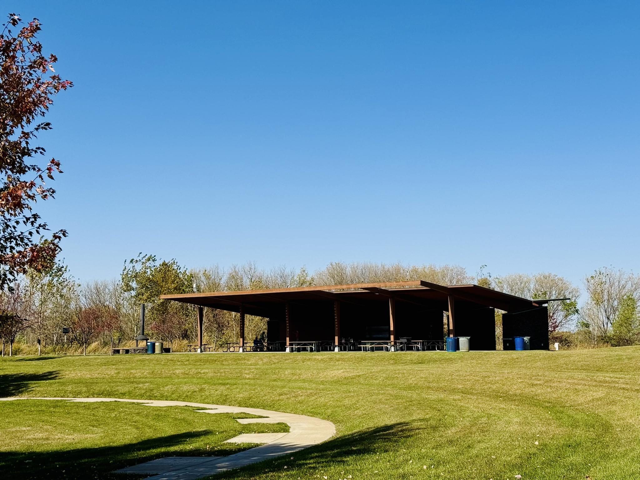 Large picnic shelter in a sunny green field under a clear blue sky.