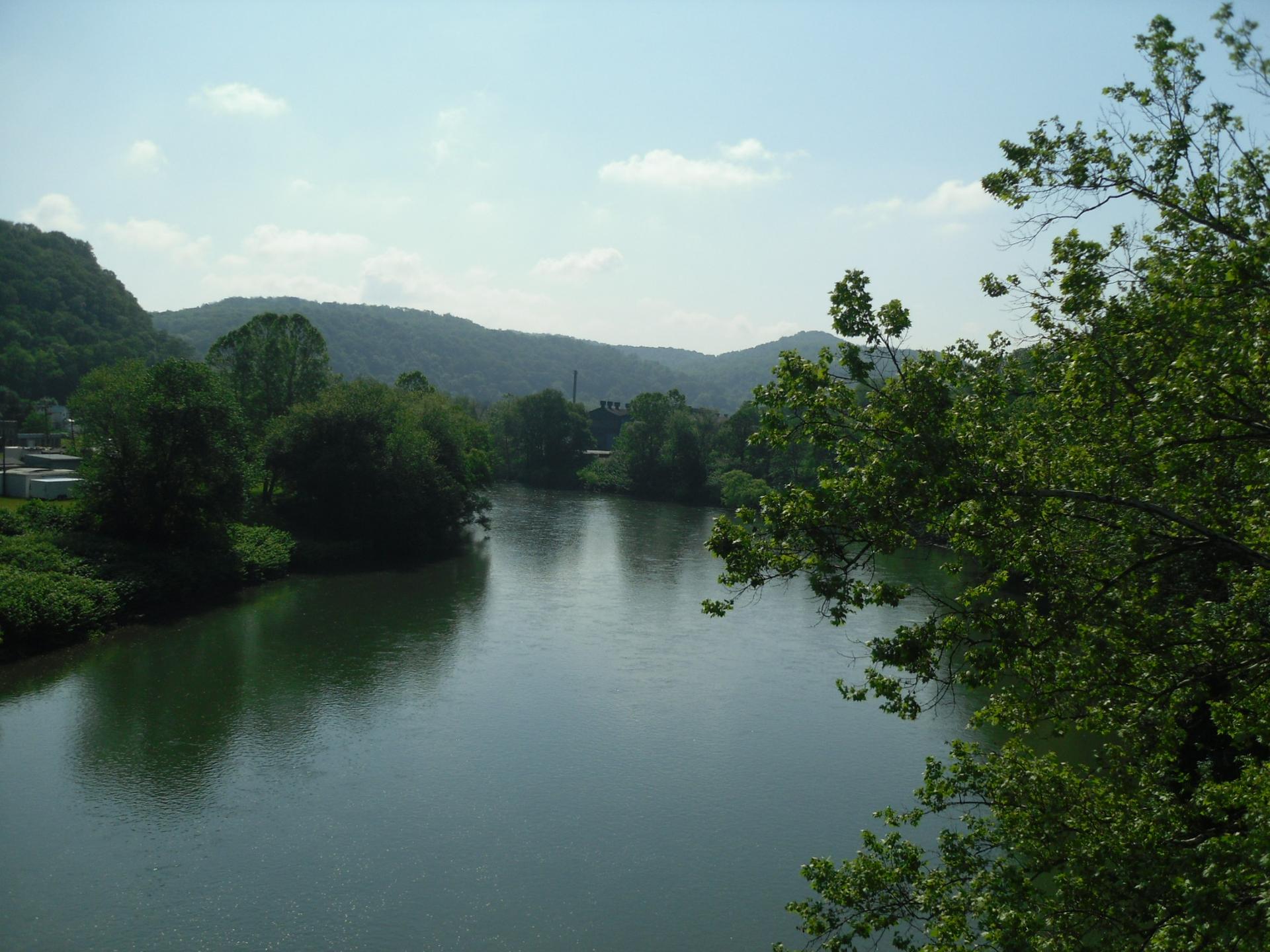 Serene river winding through a lush green valley under a bright sky.