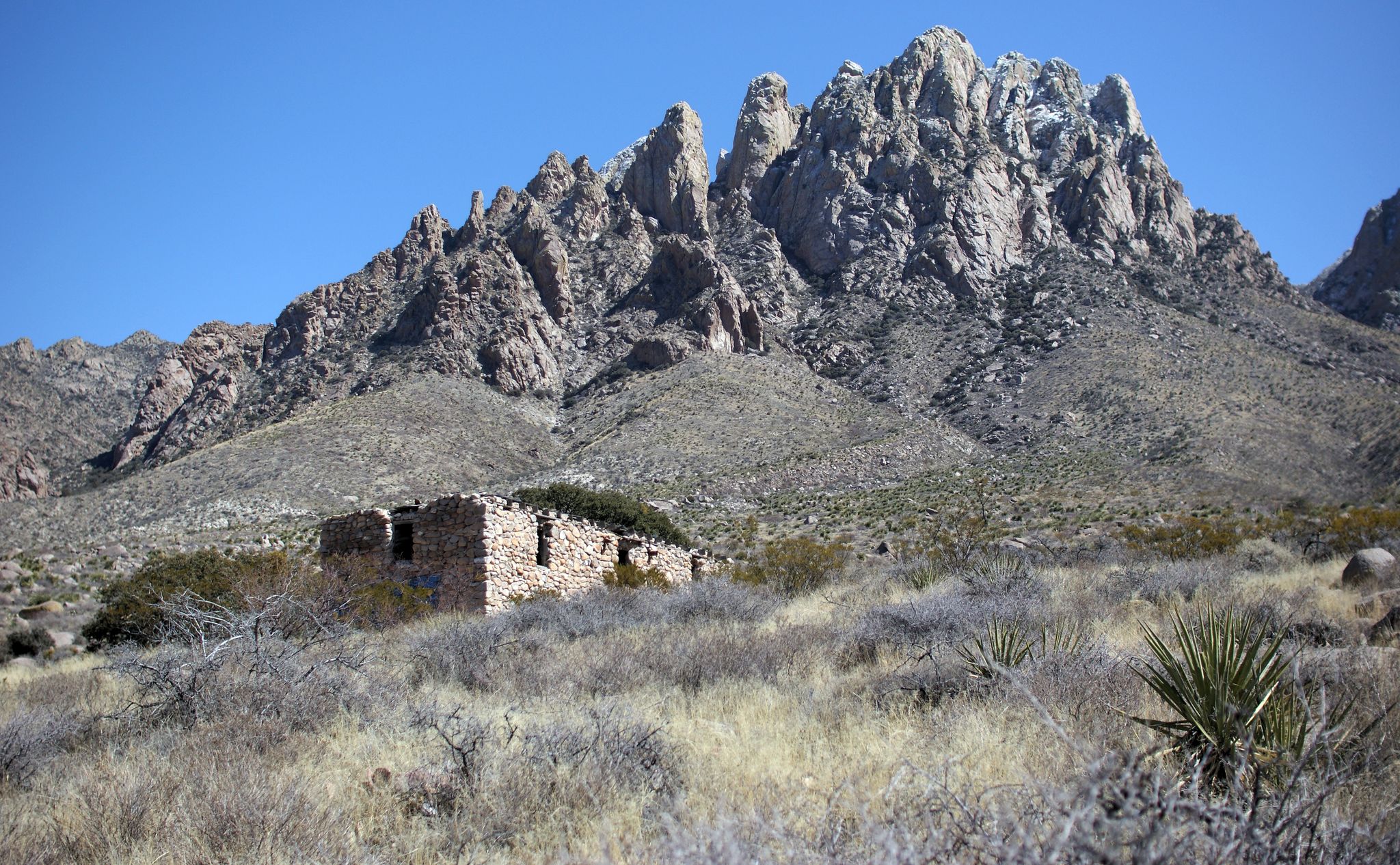 Stone ruins in an arid landscape with rugged mountains under bright sun. - Mine House Spring via Topp Hut Road