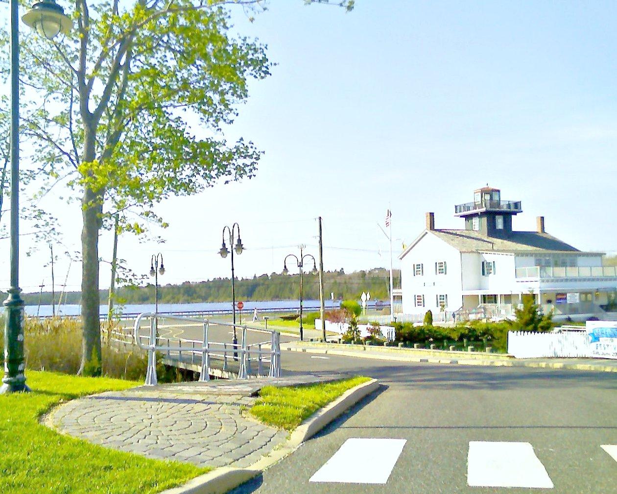 White building with cupola by water, sunny day, paved road.