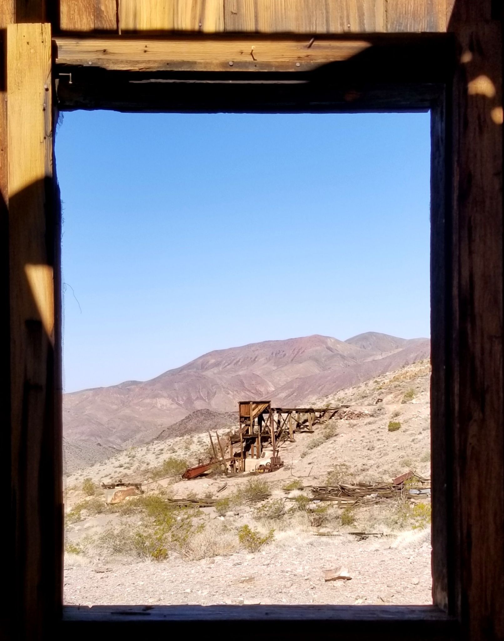 Old wooden structure on arid hills, viewed through a rustic window frame. - Echo Canyon Road to Inyo Mine