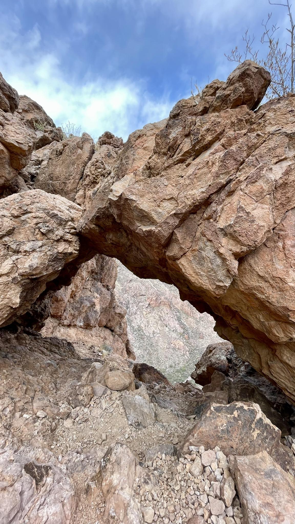 Looking up at a natural rock arch over a rocky, narrow desert path.