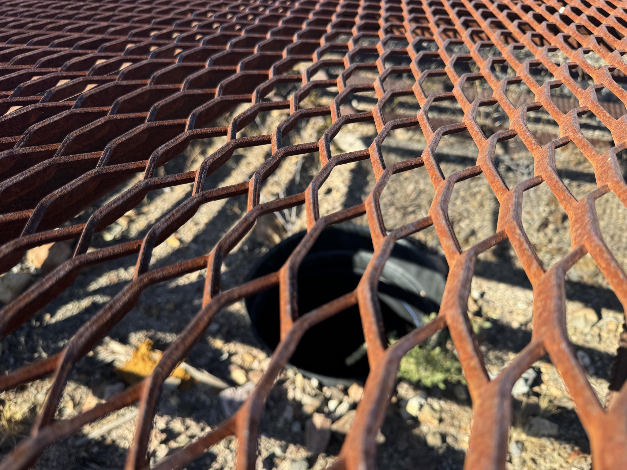 Close-up of a rusty metal grate over a dark hole in the ground.