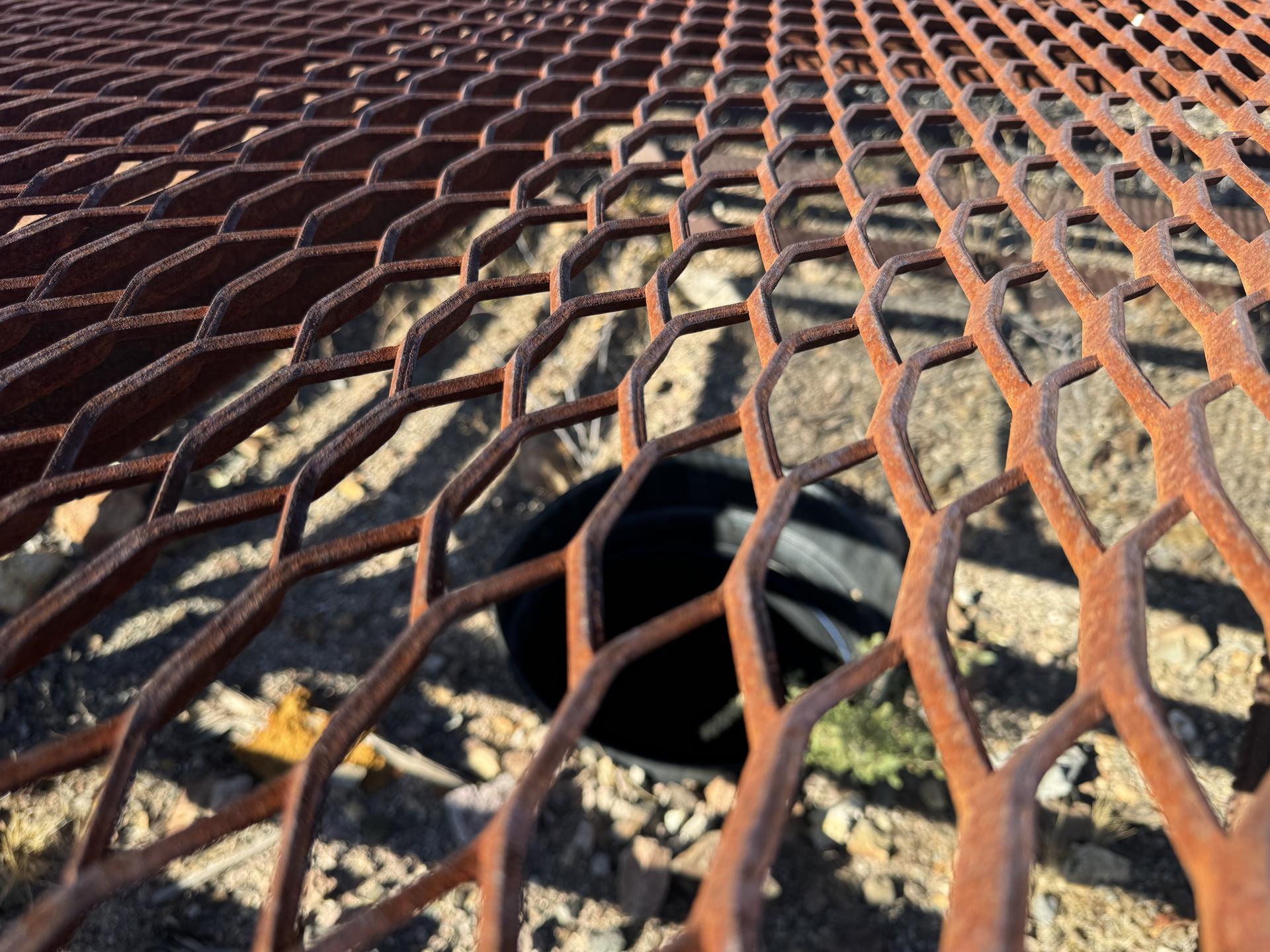 Close-up of a rusty metal grate over a dark hole in the ground.