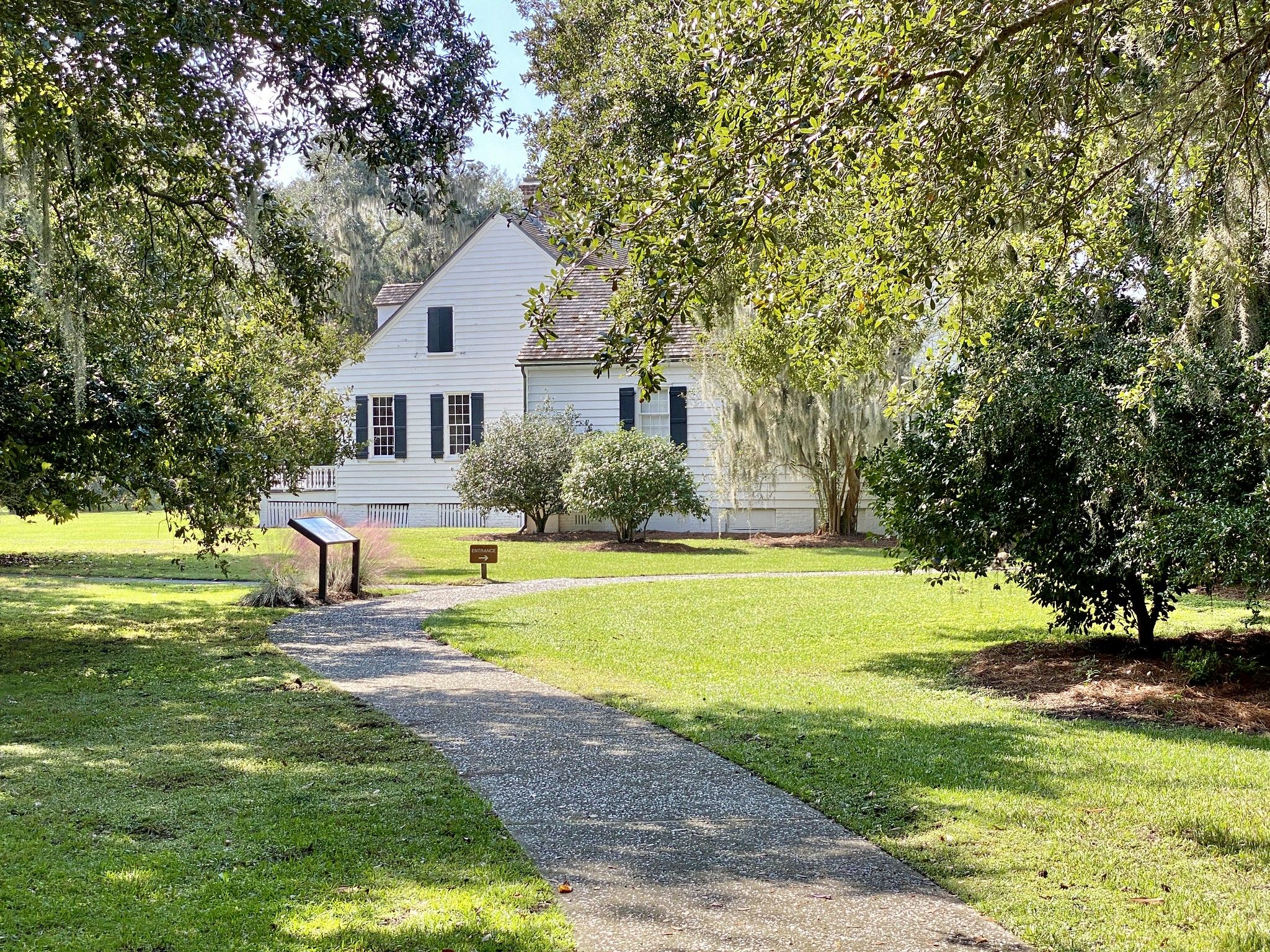 White house with dark shutters, gravel path, and sunny green lawn. - Historic Road Trace and Nature Trail