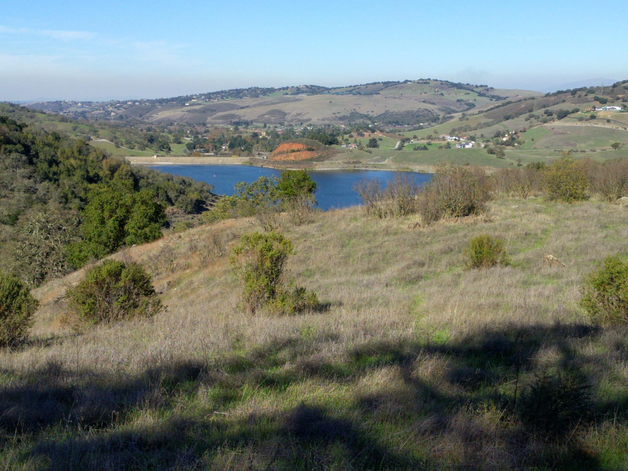 Blue lake nestled among dry, rolling hills under a clear sky.