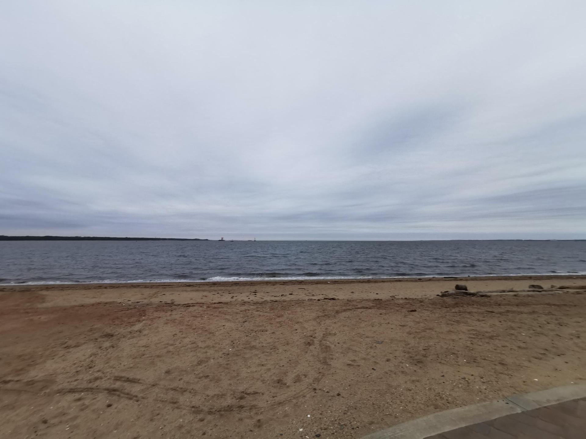 A wide sandy beach meets a calm ocean under an overcast sky.
