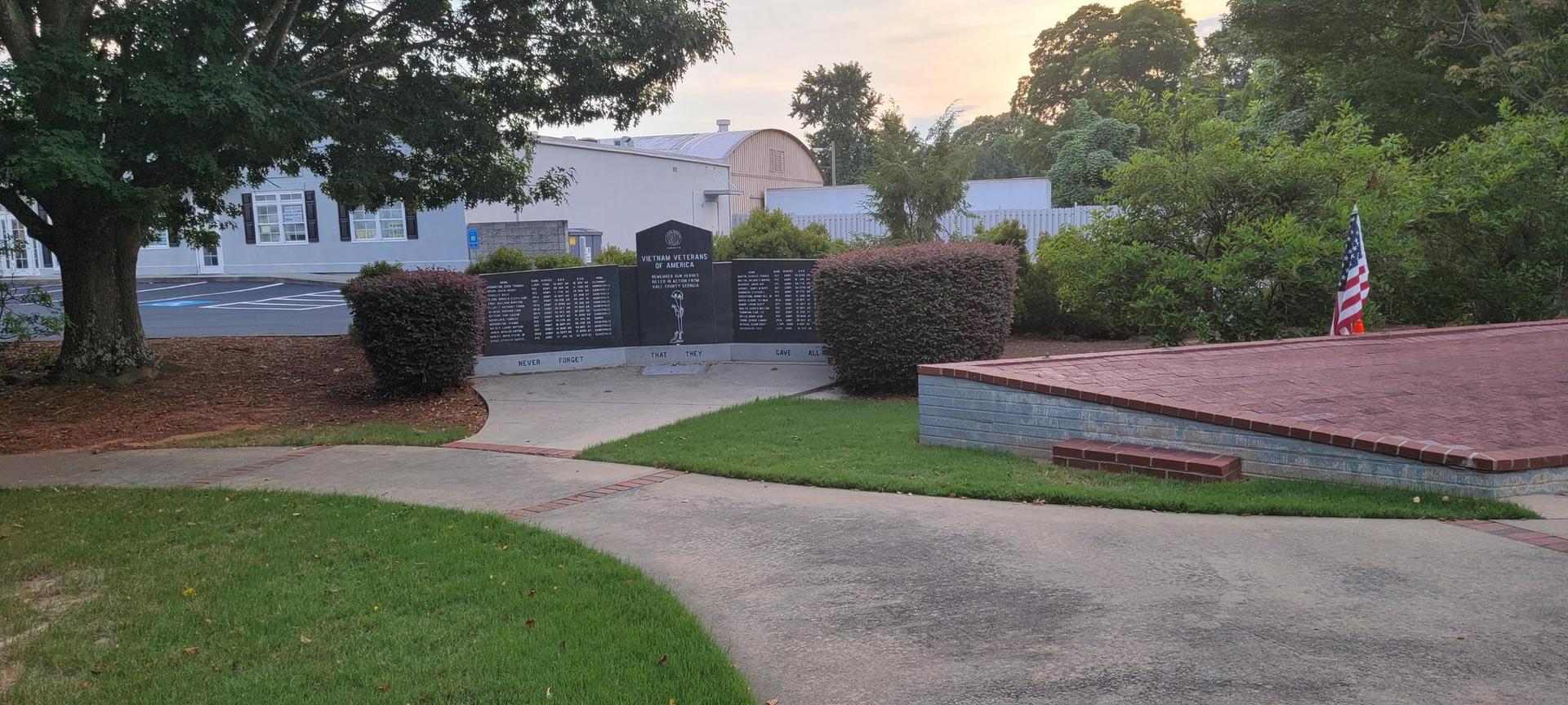 Memorial wall with an American flag, surrounded by grass and bushes.