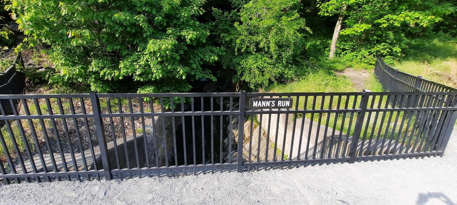 Black metal fence with a sign, green foliage, and a culvert opening.