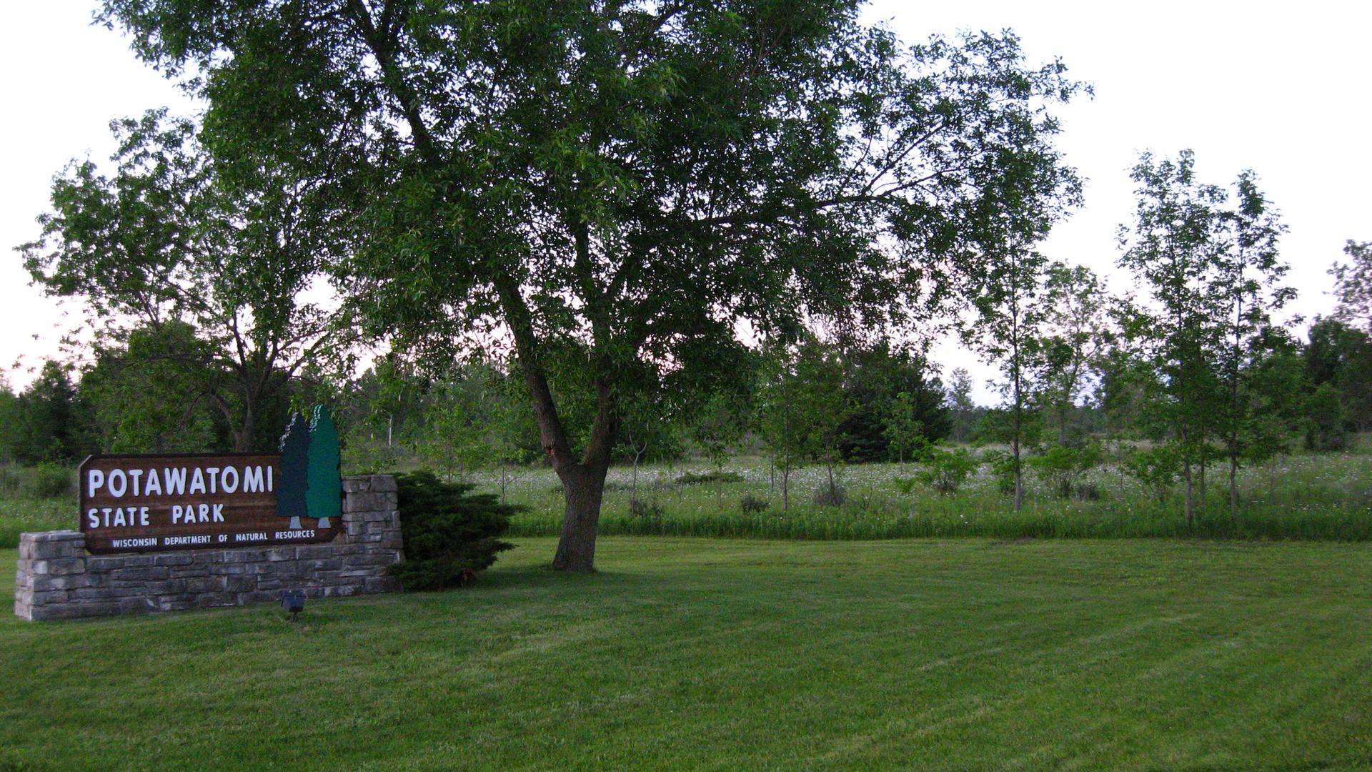 Stone and wood park sign on green grass, surrounded by trees.