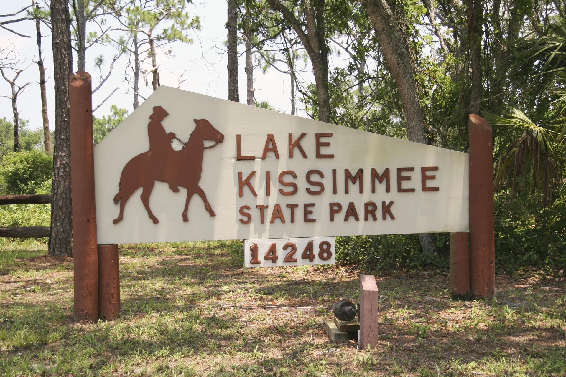 A large wooden sign with a horse and rider silhouette in a wooded area.