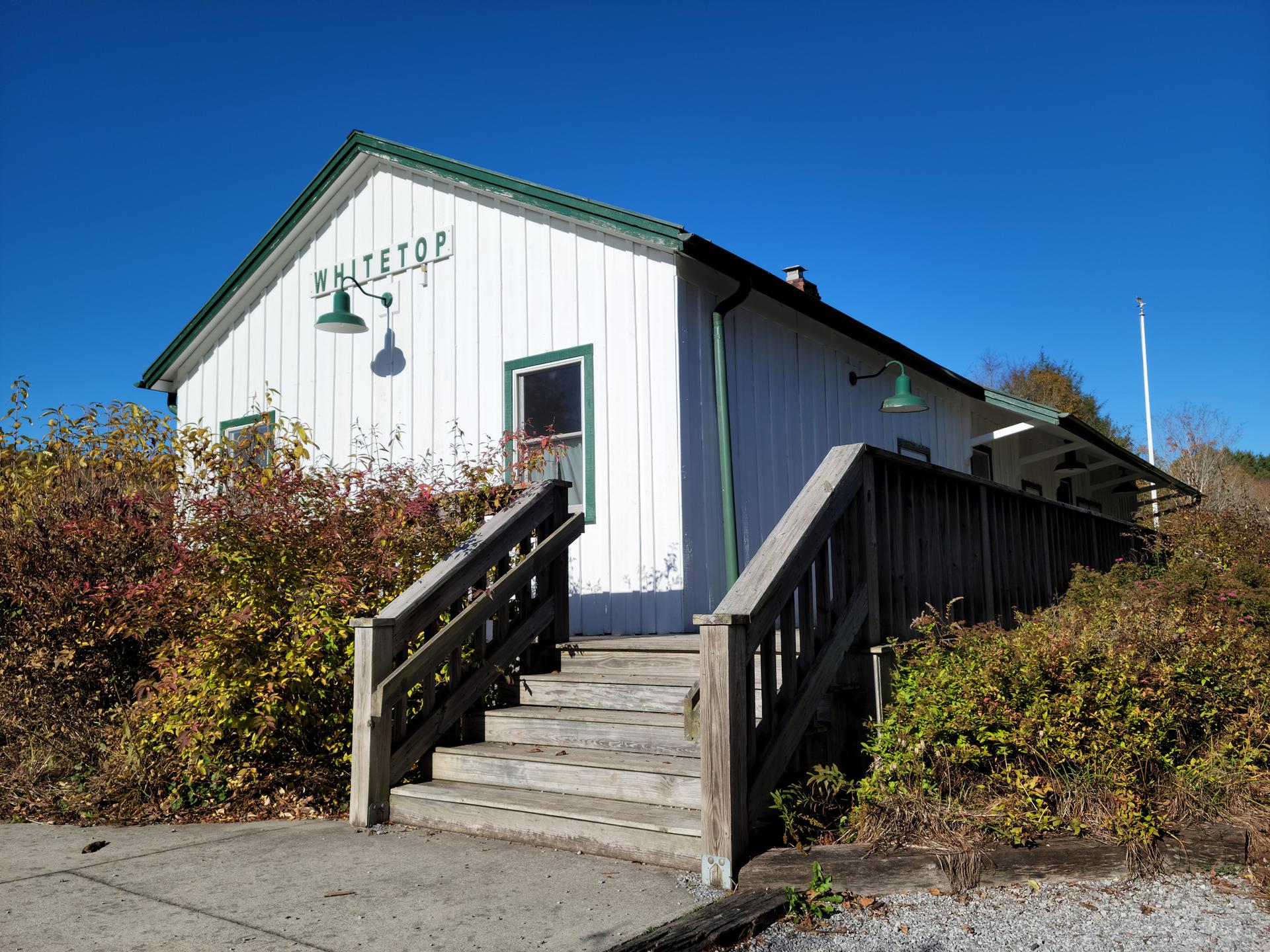 White building with green trim and wooden stairs, surrounded by autumn foliage.
