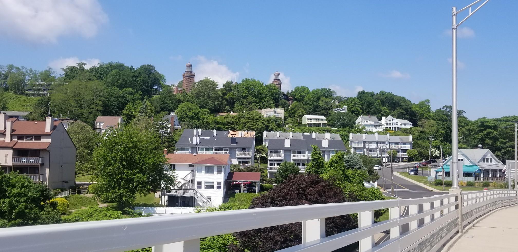 Sunny view of houses on a green hillside from a bridge railing.