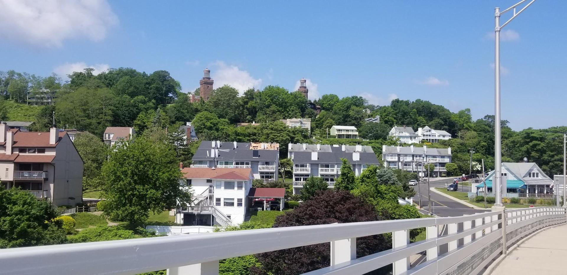 Sunny view of houses on a green hillside from a bridge railing.