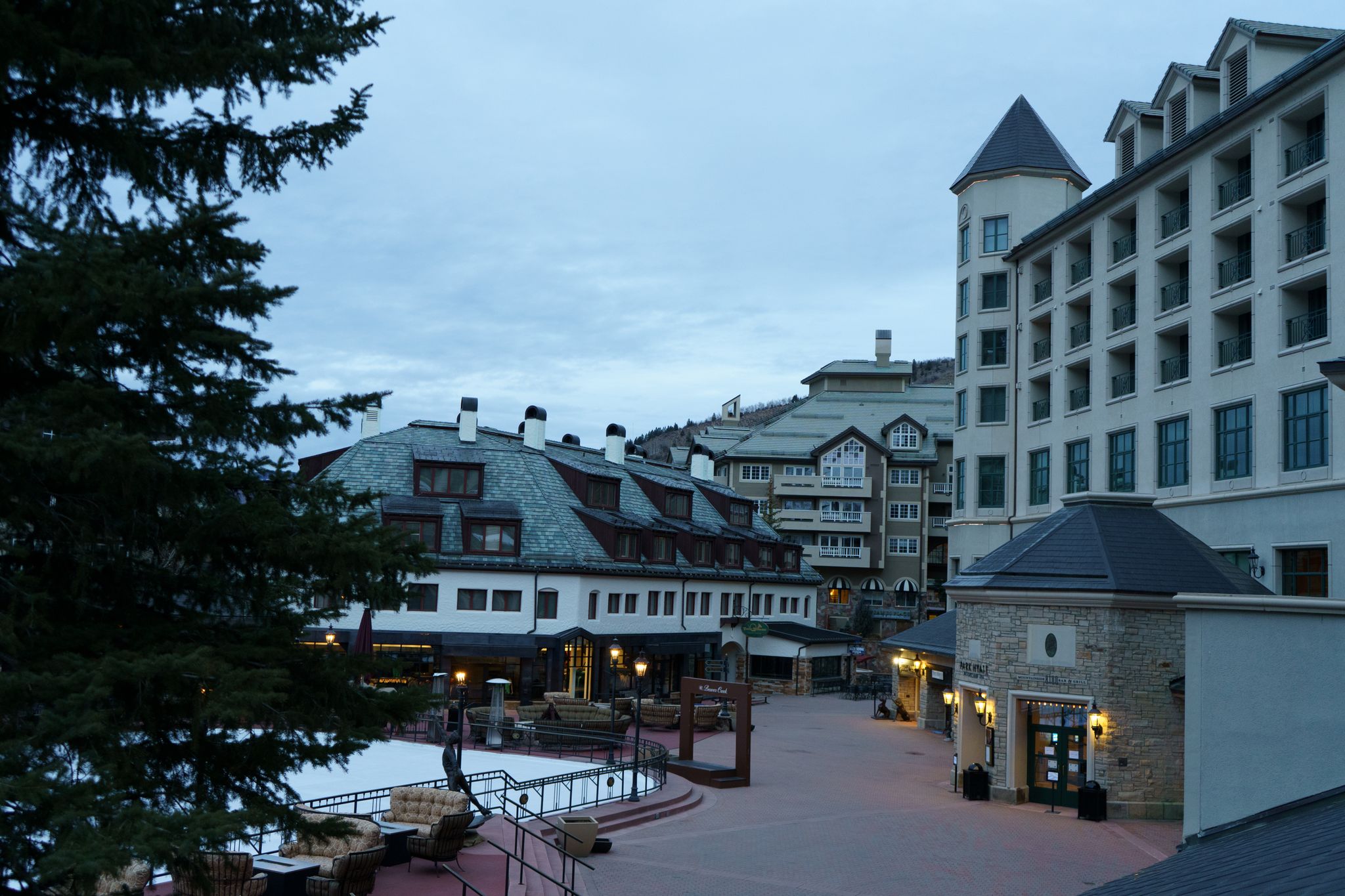 Dusk view of a quiet resort plaza with large buildings and an evergreen tree. - Moose Trail – Market Square at Beaver Creek loop from Arrowhead Village