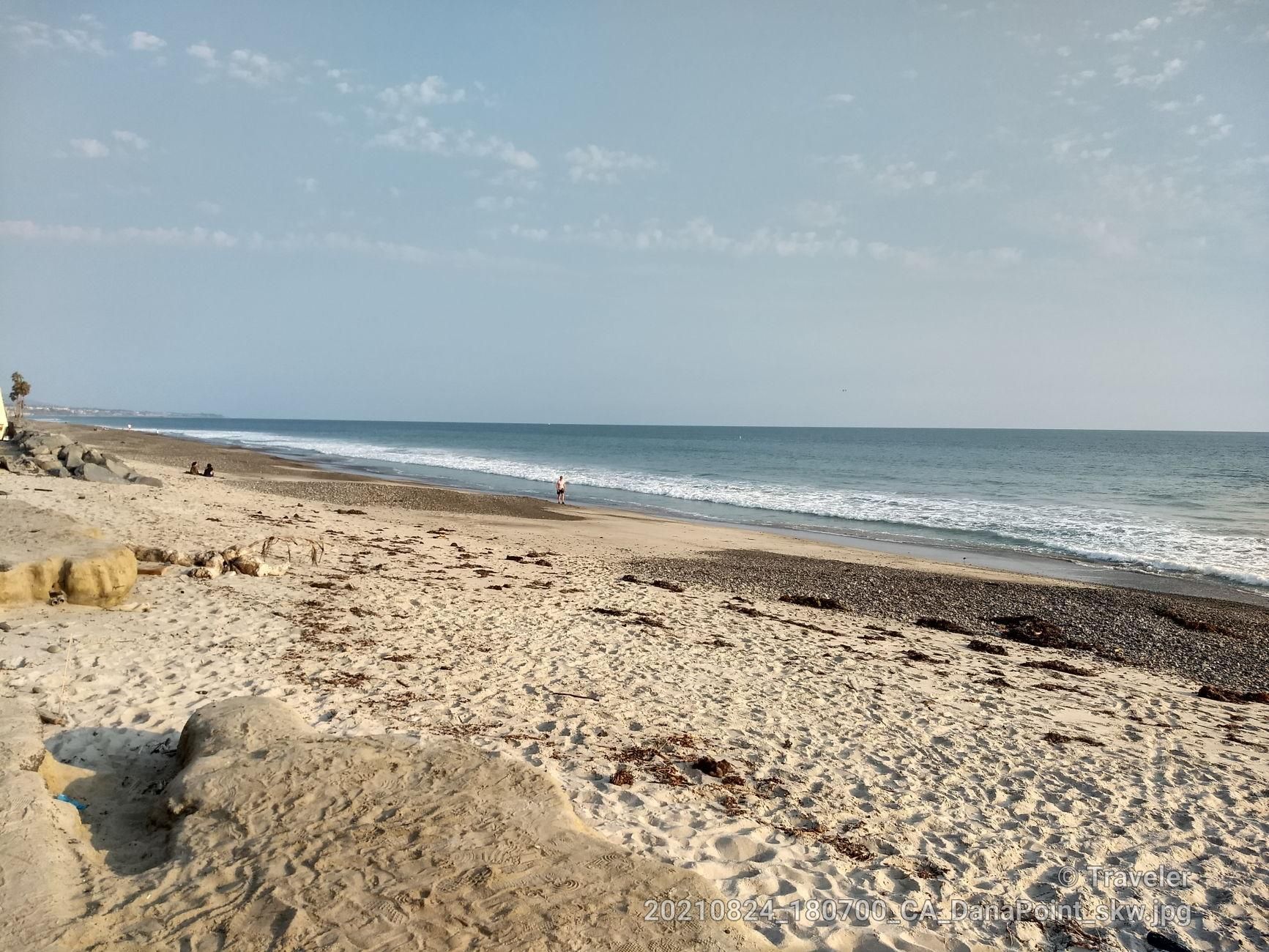 A wide sandy beach meets the ocean with gentle waves under a hazy sky. - California Mission Trail