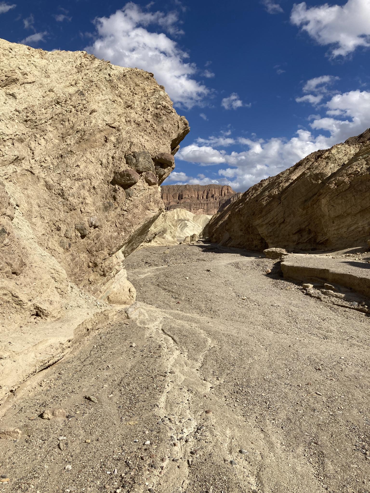 Narrow desert wash between light-colored rock walls under a partly cloudy sky.