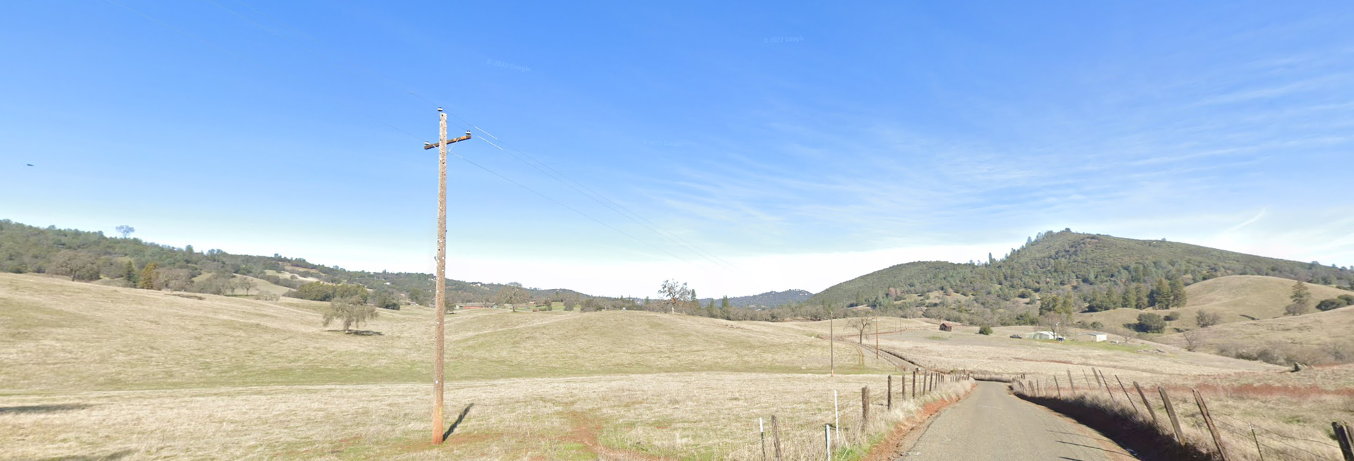 Sunny rural landscape with dry grassy hills, a dirt road, and a power pole.