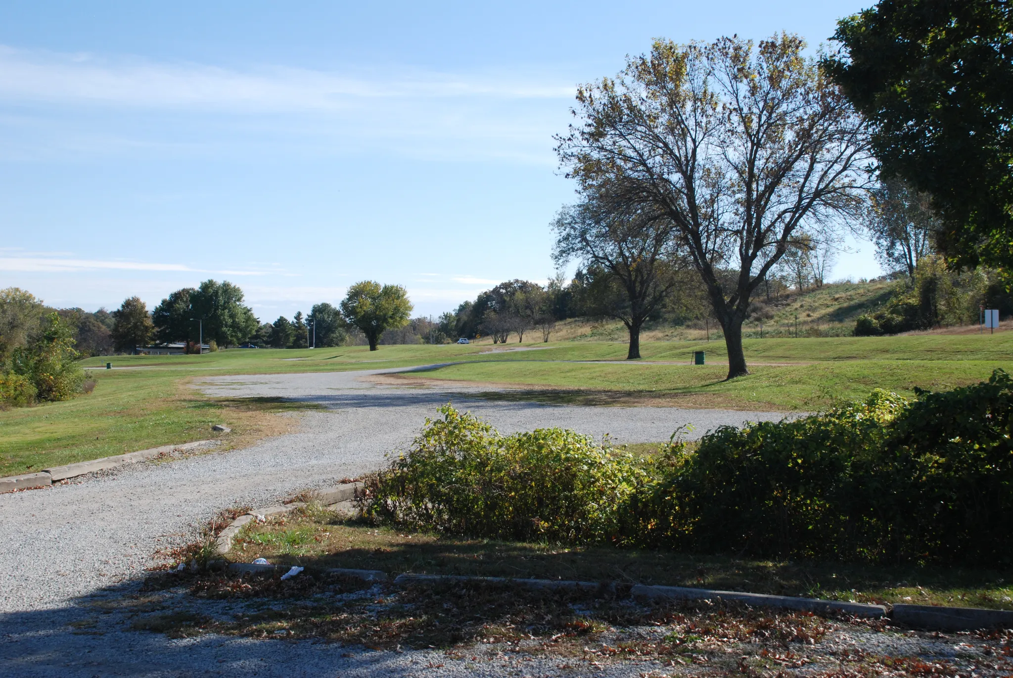Wide gravel parking area next to a grassy field with scattered trees. - Rock Ledges Loop